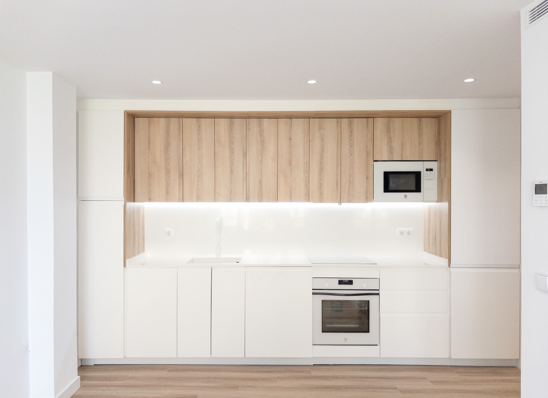 Cocina minimalista blanca con muebles altos de madera clara