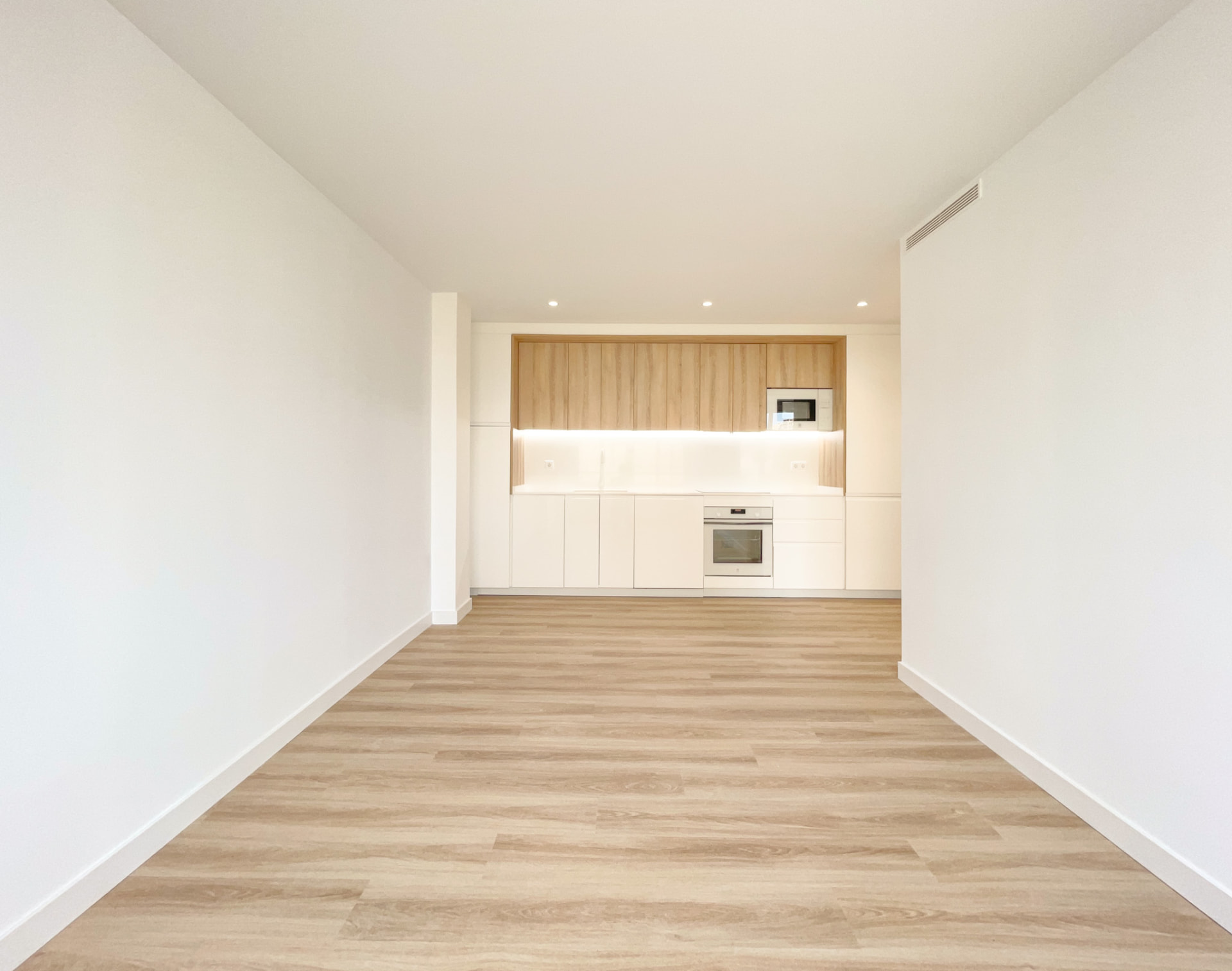 Estudio diáfano de suelo de madera con cocina blanca integrada al fondo
